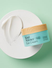 Eye Cream product with a swipe of white cream on a round surface, on a mint green background
