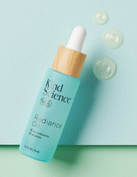 Kind Science Radiance Oil product on a pastel blue surface with floating gel bubbles