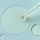 Glass dropper releasing a clear liquid drop on a pale blue background