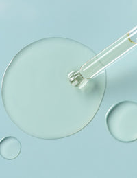 Glass dropper releasing a clear liquid drop on a pale blue background