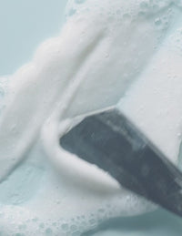 Foamy white cleanser being smoothed across a light blue surface