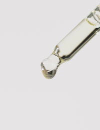 Close-up of a glass dropper releasing a clear liquid droplet against a white background